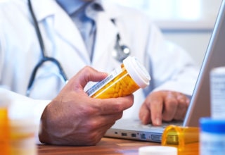 pharmacist holding a bottle of medicine while typing in his laptop
